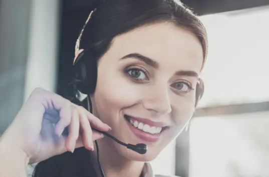 Donna sorridente che indossa una cuffia con microfono, con il microfono vicino alla bocca, seduta al chiuso e che guarda verso la telecamera; probabilmente lavora nel servizio clienti o presso un call center della Sabina Robotics. Donna sorridente che indossa una cuffia con microfono, con il microfono vicino alla bocca, seduta al chiuso e che guarda verso la telecamera; probabilmente lavora nel servizio clienti o presso un call center della Sabina Robotics.